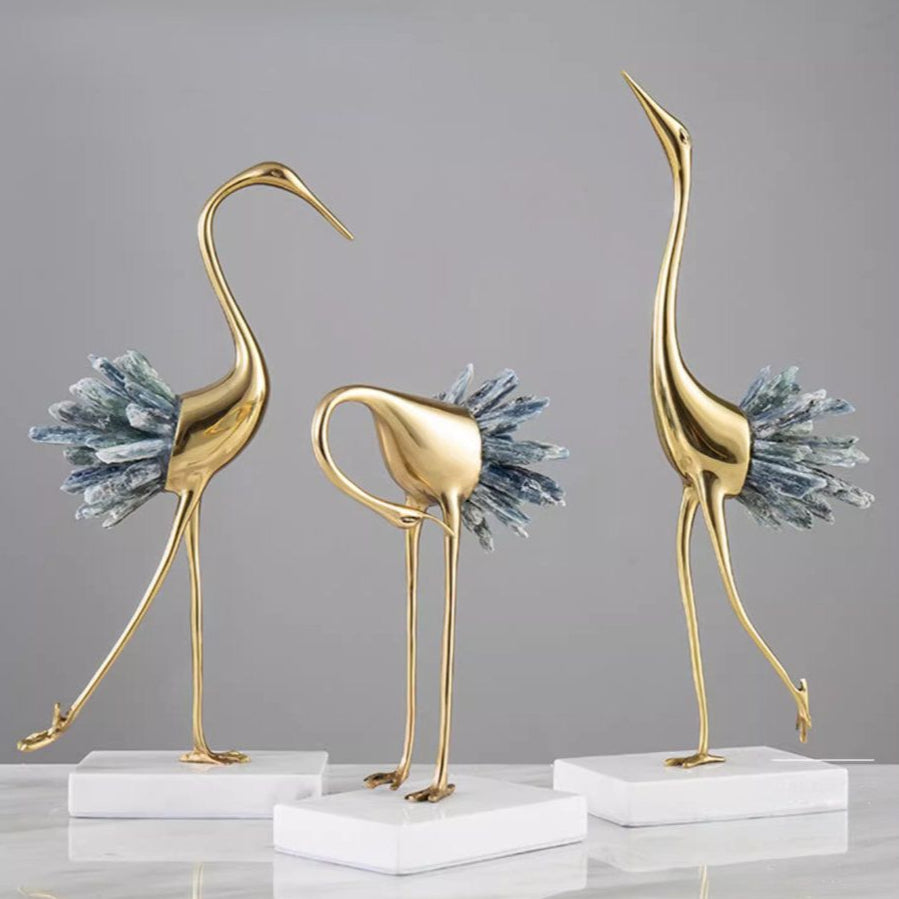 Set of three gold bird sculptures on white bases against a gray background