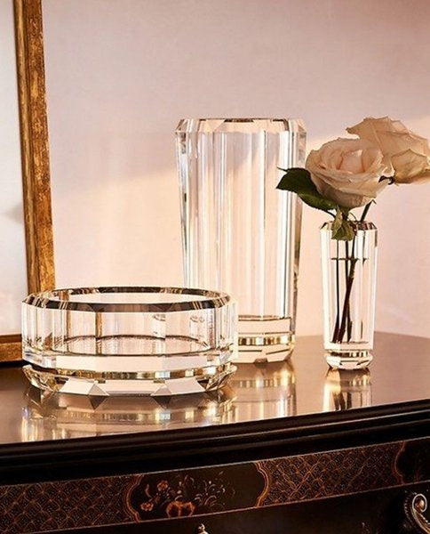 Decorative glass bowl and vase with a white rose on a reflective surface.